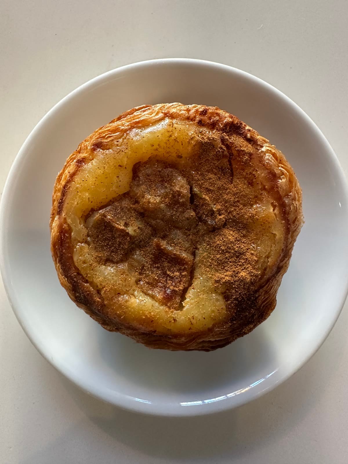 A cinnamon apple pastel de nata on a white plate, dusted with cinnamon